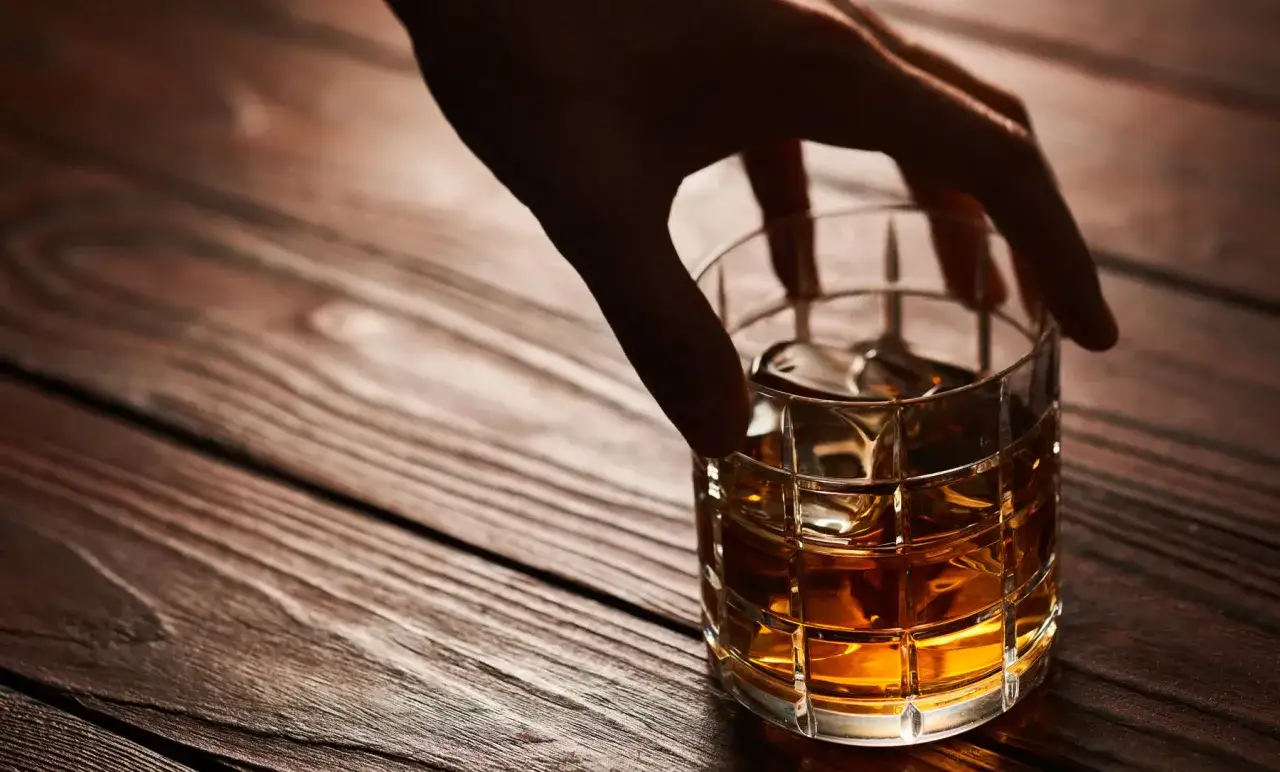Hand greift nach einem Glas Whisky mit Eis. Die ideale Trinktemperatur f&uuml;r Whisky ist erreicht.