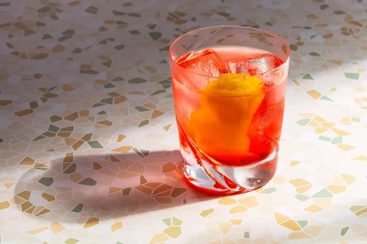 Ein erfrischender Drink mit Campari, Gin und einer Orangenscheibe, serviert auf einem Mosaiktisch.