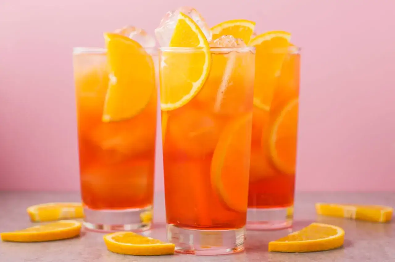 Drei erfrischende Aperol Spritz mit leuchtendem Aperol Farbstoff, Eis und Orangenscheiben, garniert mit frischen Orangenspalten.