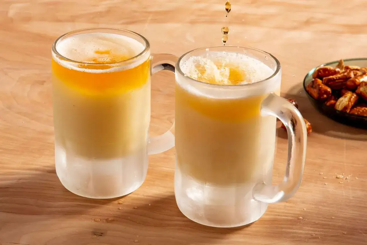 Zwei Gläser mit eisgekühltem Ginger Beer mit Alkohol und einer Schaumkrone. Daneben eine Schale mit Brezeln.