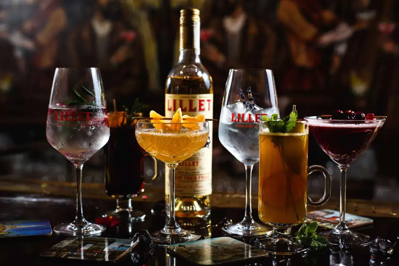 Fünf farbenfrohe Cocktails und eine Flasche Lillet stehen bereit. Erfahren Sie, wie schmeckt Lillet – erfrischend, fruchtig und vielseitig.