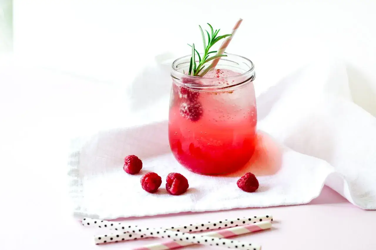 Erfrischender Gin Tonic mit Himbeeren, garniert mit Rosmarin und einem rosa-weißen Strohhalm.