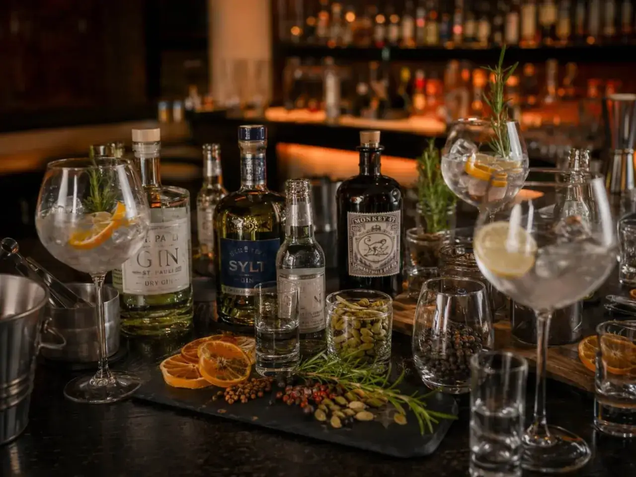 Gin tasting: Flaschen, Gläser mit Eis, Zitrone und Rosmarin, sowie Gewürze wie Wacholderbeeren und Kardamom.