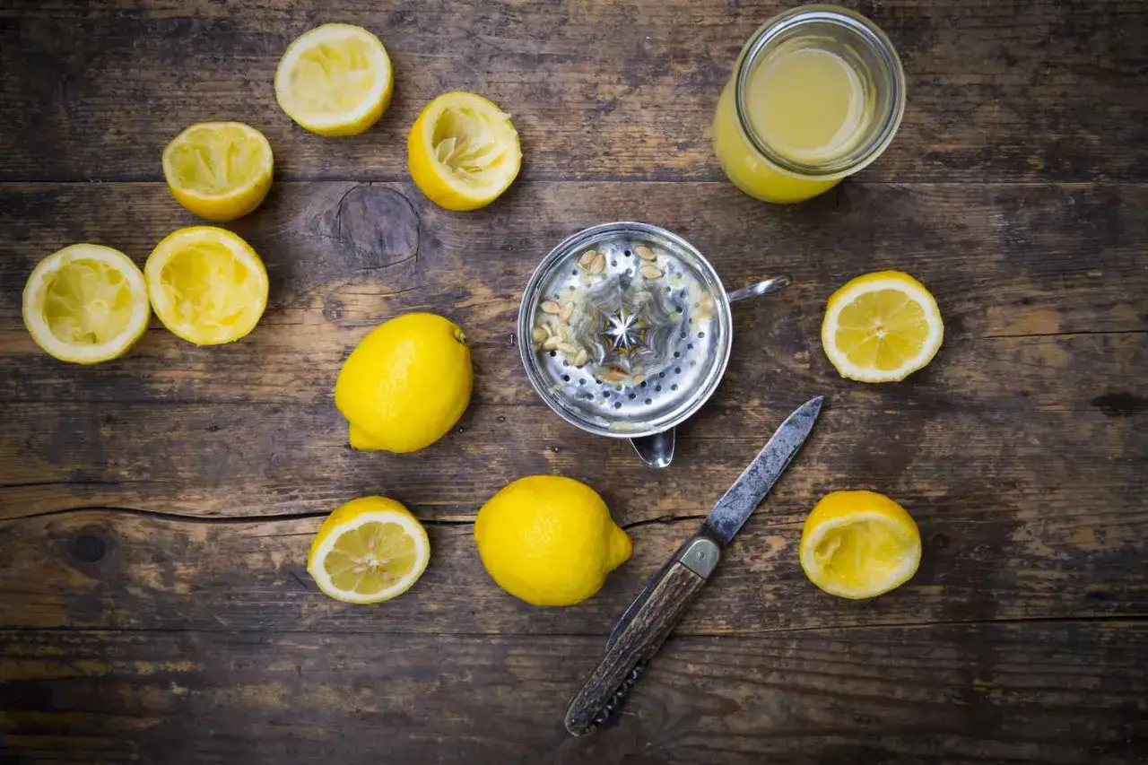 Frische Zitronen, ausgepresste Hälften, ein Entsafter und ein Glas Zitronensaft – alles bereit für den perfekten zitronensaft ersatz.