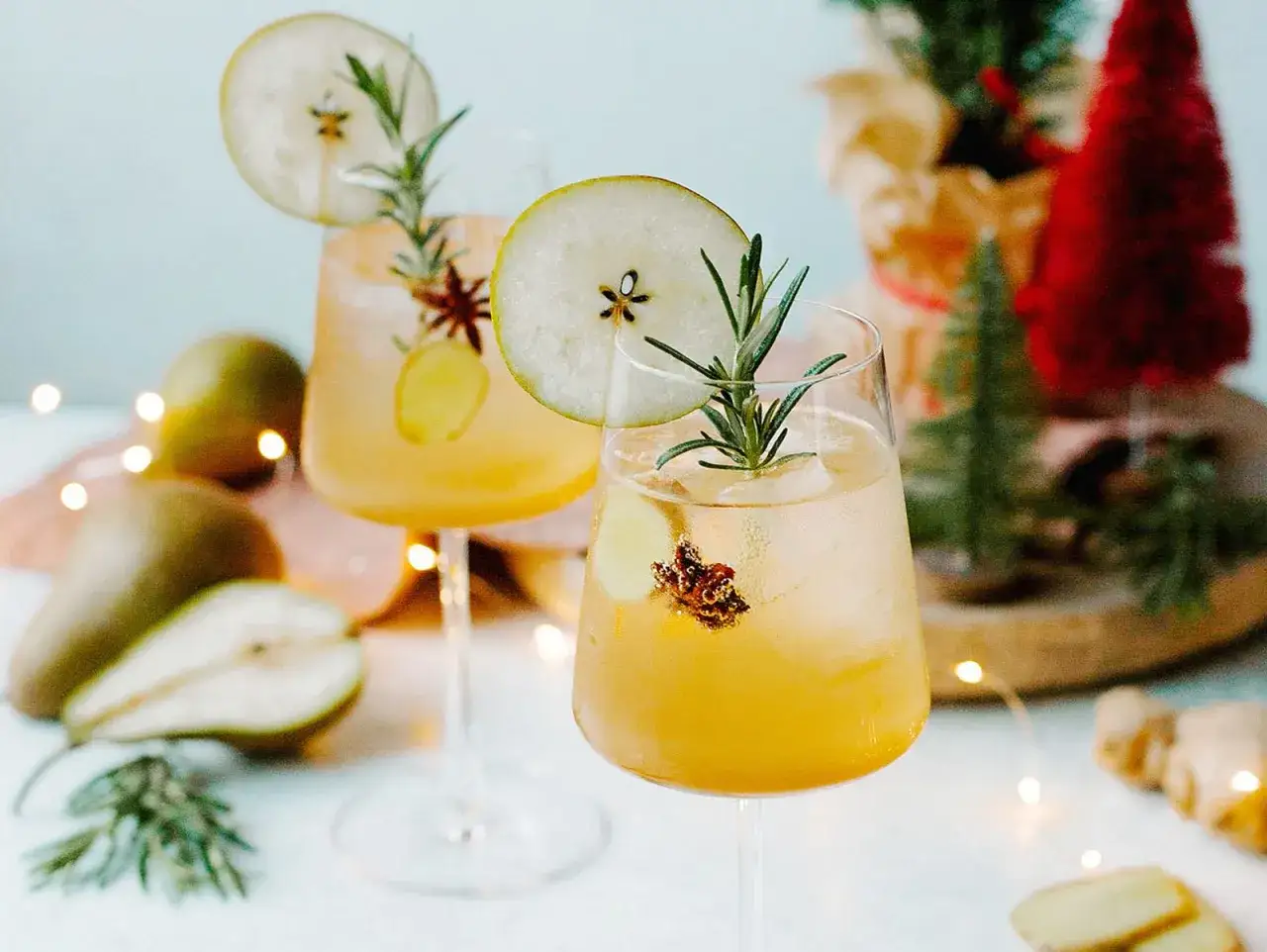 Zwei festlich dekorierte Gläser mit einem erfrischenden Birnen Spritz, garniert mit Birnenscheiben und Rosmarin.