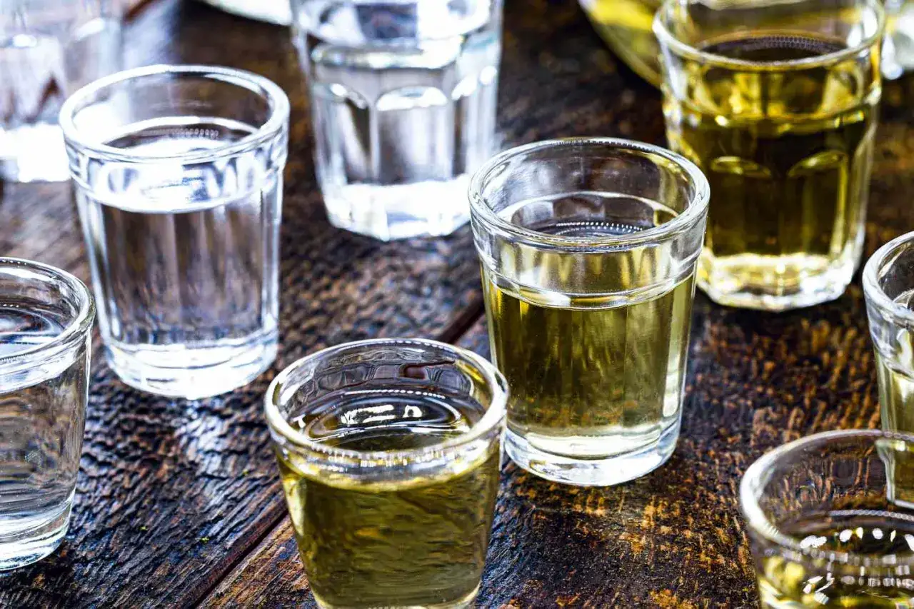 Mehrere Gläser mit klarem und goldenem Cachaca Rum stehen auf einem rustikalen Holztisch.