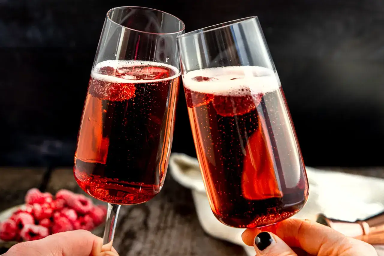 Zwei Gläser Kir Royal stoßen an, mit frischen Himbeeren und prickelndem Champagner. Ein perfektes Rezept für besondere Anlässe.
