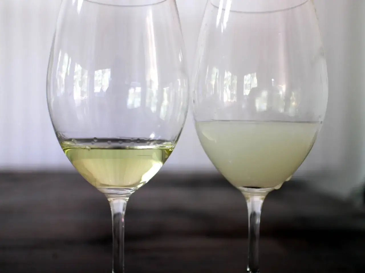 Zwei Weingläser: eins mit klarem, gelblichem Inhalt, das andere mit trübem, milchigem Inhalt, der an Ouzo Geschmack erinnert.