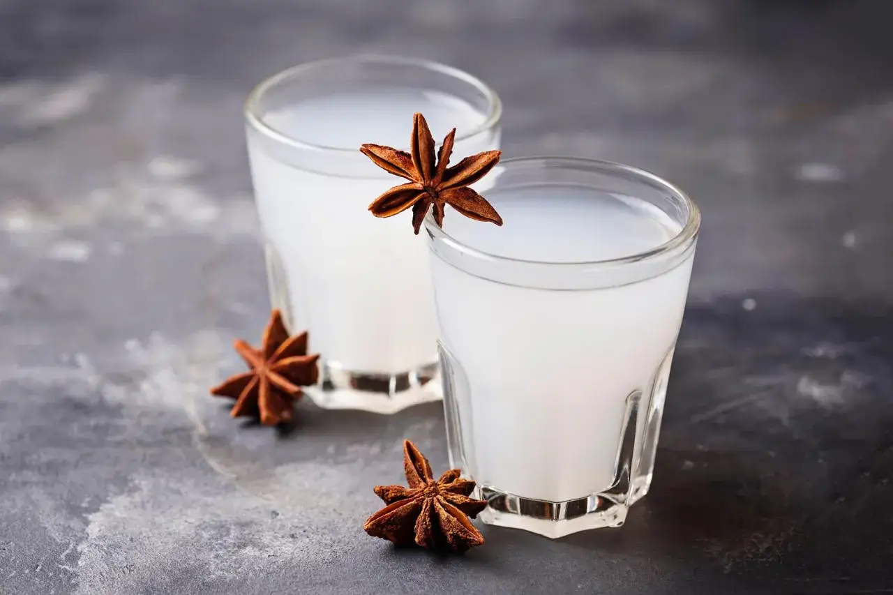 Zwei Gläser Ouzo mit Sternanis. Der Ouzo hat einen hohen Alkoholgehalt, erkennbar an der milchigen Trübung.