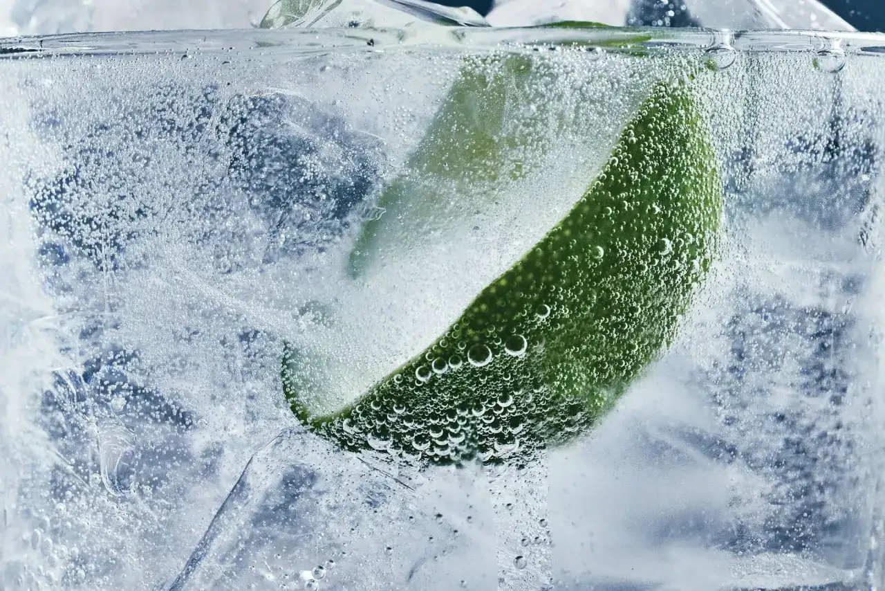 Erfrischendes chinin tonic water mit Eis und einer Limettenspalte, umgeben von sprudelnden Bläschen.