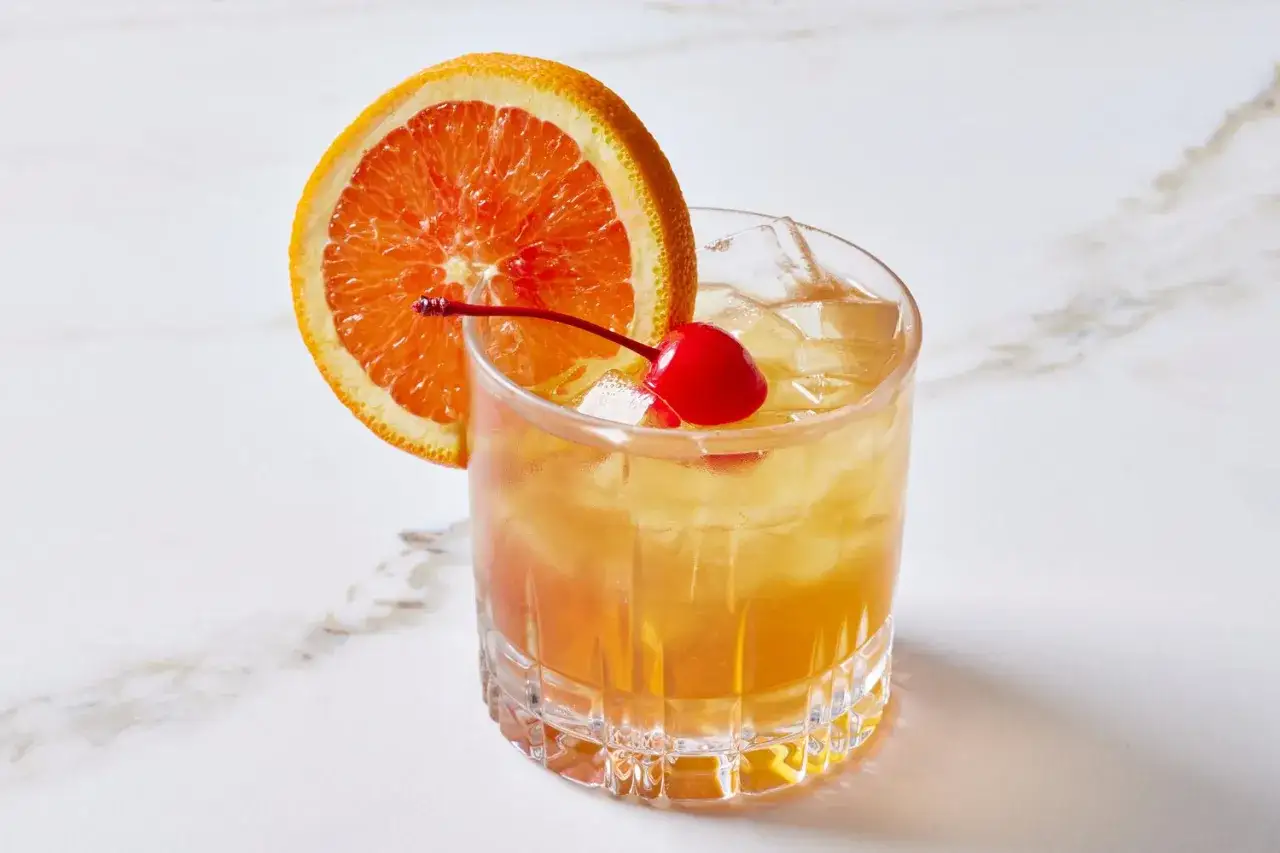 Ein erfrischender Amaretto Sour mit Eis, garniert mit einer Orangenscheibe und einer Kirsche.