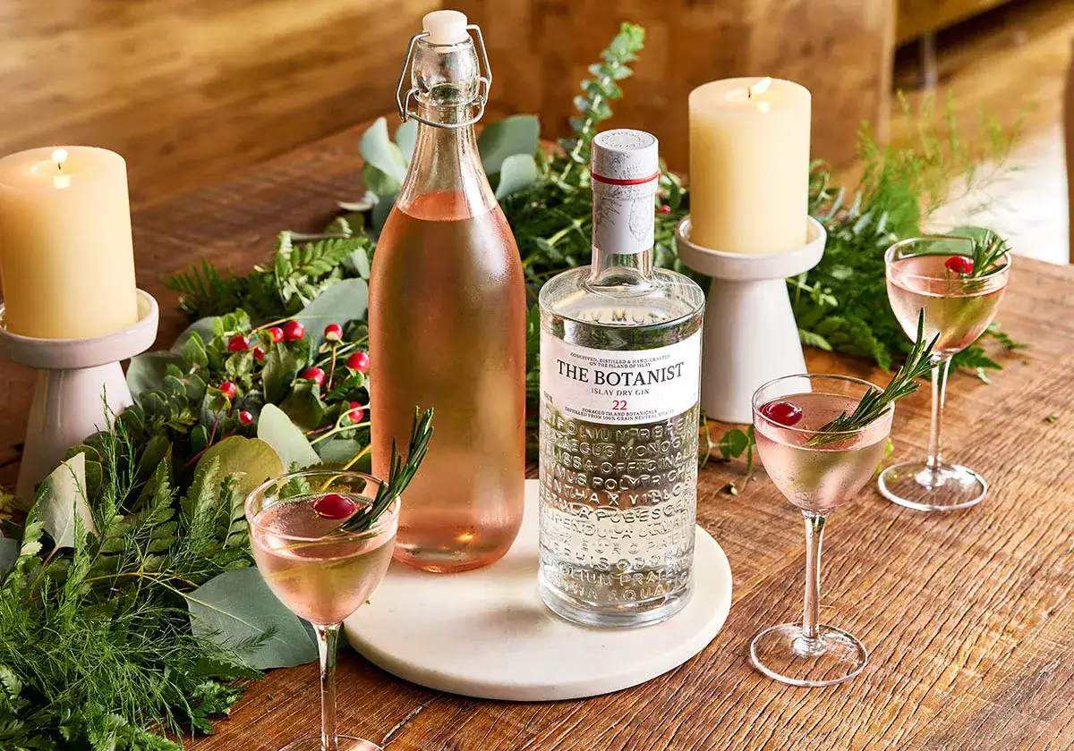 The Botanist Gin: festlich gedeckter Tisch mit Kerzen, gr&uuml;nen Zweigen und zwei eleganten Cocktails. So kann man den Gin genie&szlig;en.