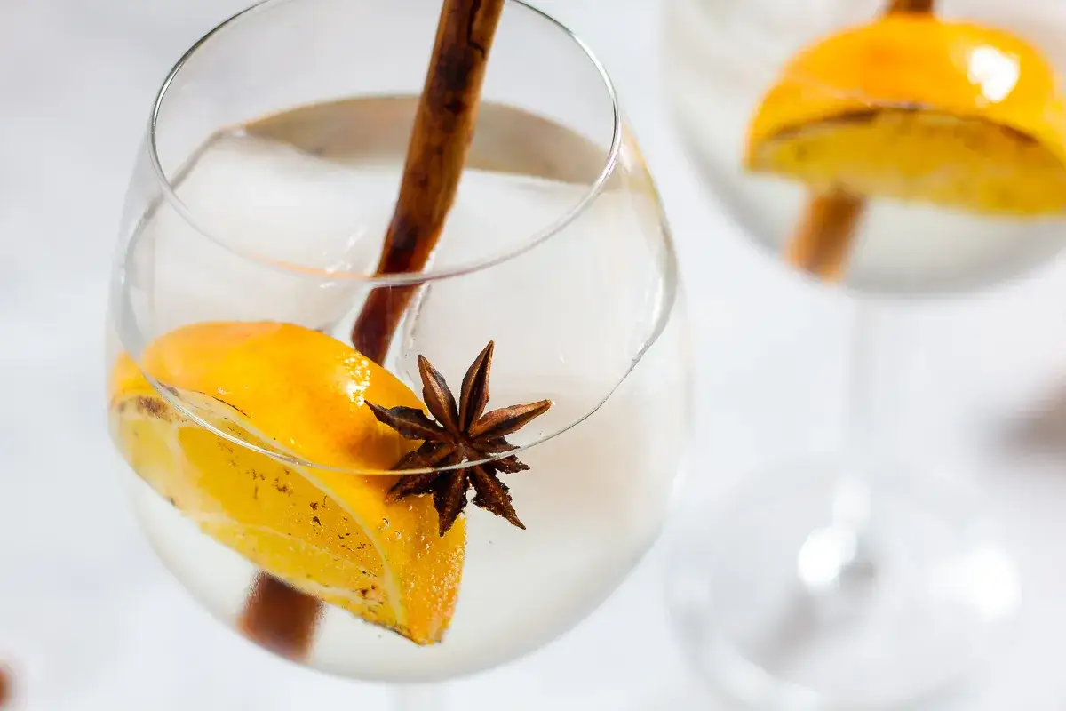 Ein Glas mit Eis, Orangenscheibe, Zimtstange und Sternanis. So könnte man sich vorstellen, wie schmeckt anis in einem erfrischenden Drink.