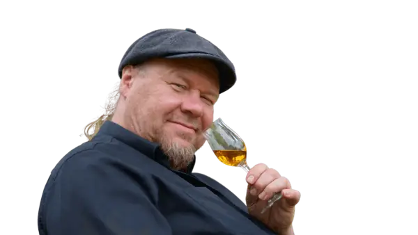 Ein Mann mit Schiebermütze und Bart hält ein Glas bernsteinfarbenen Rum. Er scheint zu wissen, wie man Rum genießt.