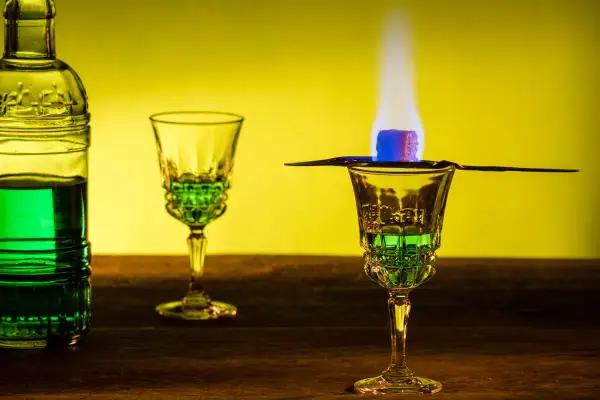 Grüner Absinth brennt in einem Glas, ein Zuckerwürfel karamellisiert. Die Zubereitung erinnert an die traditionelle Absinth Herkunft.