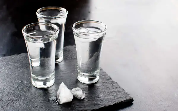 Drei Gläser Wodka mit Eiswürfeln auf schwarzem Schiefer. Wodka wird aus Getreide oder Kartoffeln hergestellt.