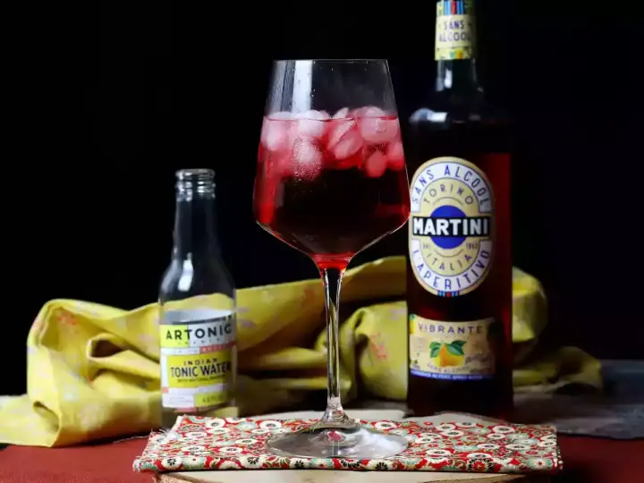 Ein Glas mit einem roten, eisgekühlten Getränk steht neben einer Flasche Martini alkoholfrei und Tonic Water.